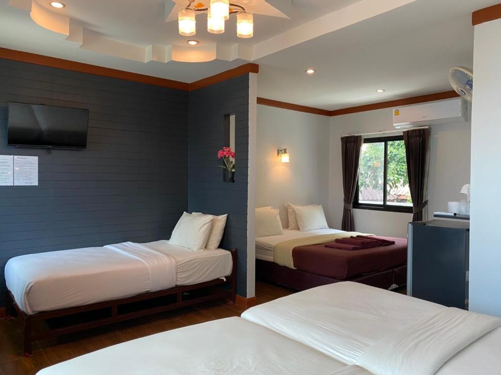 ห้องพักในโรงแรมที่มีเตียงสามเตียง ทีวีติดผนัง ตู้เย็นขนาดเล็ก เครื่องปรับอากาศ หน้าต่างพร้อมม่าน และพื้นไม้ — เป็นตัวเลือกที่สะดวกสบายสำหรับผู้ที่มองหาที่พักเกาะเสม็ดติดทะเล หรือประสบการณ์การพักผ่อนที่ผ่อนคลายบนเกาะเสม็ด.