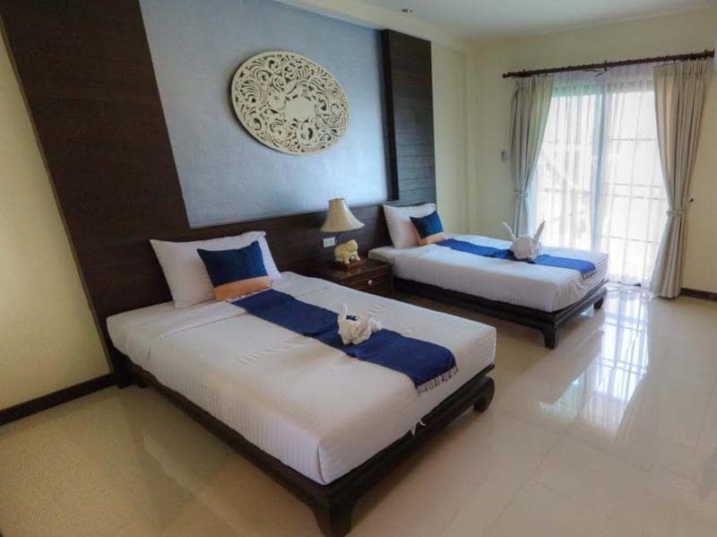 เตียงสองเตียงในห้องที่มีผ้าปูที่นอนสีขาวและผ้าห่มสีน้ำเงิน ที่พักน่าน