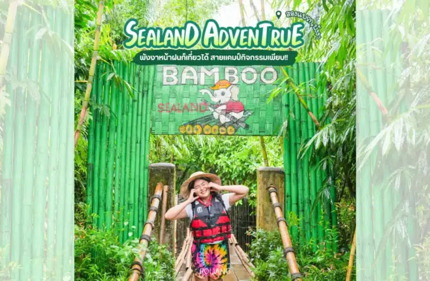 บุคคลที่สวมชุดสำหรับกิจกรรมกลางแจ้งโพสท่าและยิ้มอยู่หน้าป้ายทางเข้าธีมไม้ไผ่สีเขียวที่เขียนว่า "BAMBOO SEALAND" ที่ซีแลนด์แอดเวนเจอร์ พังงา.