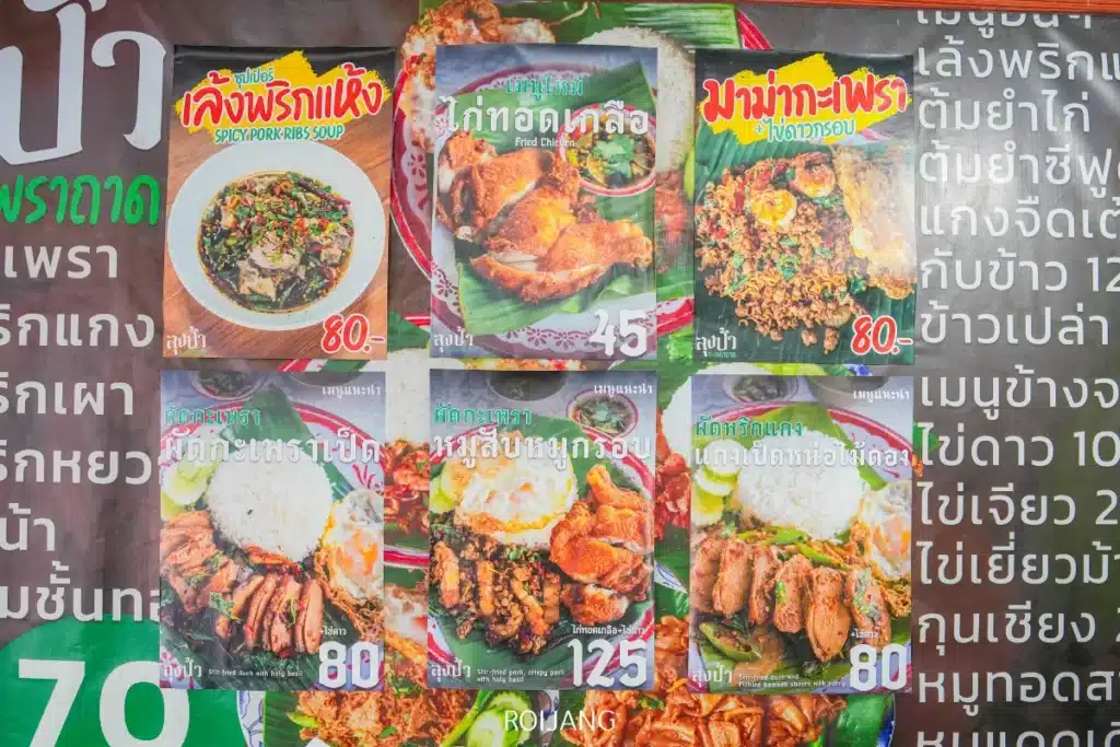 อาหารไทยหกจาน รวมถึง ลุงป้ากะเพราถาด พร้อมชื่อ คำอธิบาย และราคาที่แสดงบนกระดานเมนูพื้นหลังสีเขียวพร้อมข้อความภาษาไทย.