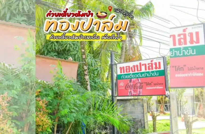 ป้ายร้านอาหารภาษาไทย รวมถึง ทองปาล์มก๋วยเตี๋ยวต้มยำน้ำข้น ถูกจัดแสดงท่ามกลางต้นไม้สีเขียว โฆษณาบะหมี่และโปรโมชั่นโคคา-โคล่าใกล้ทางเข้า.