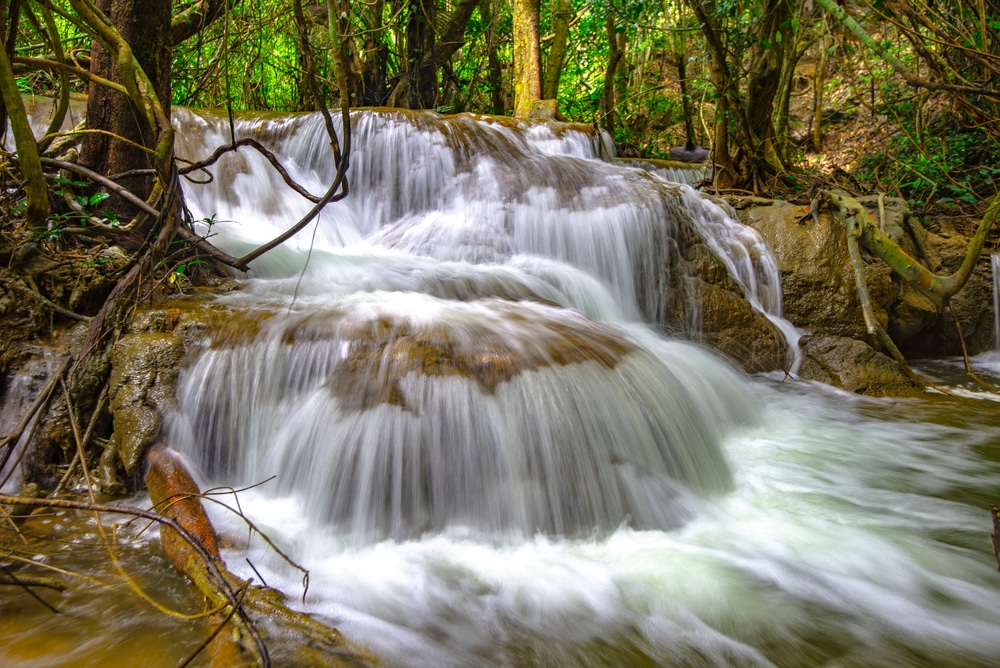 น้ำตกขนาดเล็กไหลลดหลั่นลงมาตามโขดหินที่โอบล้อมด้วยพืชพรรณเขียวชอุ่มในบรรยากาศป่าไม้ ทำให้ที่นี่กลายเป็นหนึ่งในสถานที่ท่องเที่ยวลับสำหรับผู้ต้องการเที่ยวกาญจนบุรีและสำรวจสถานที่ท่องเที่ยวในกาญจนบุรี.