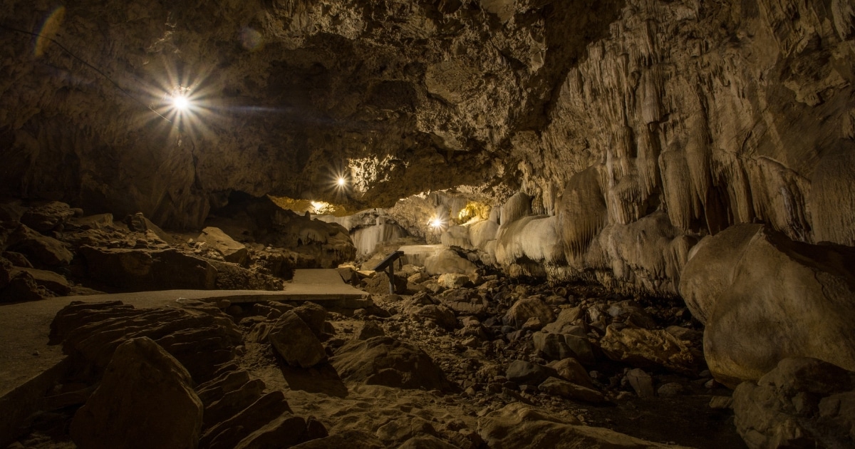 ภายในถ้ำใต้ดินที่มีผนังหิน, หินย้อย, หินงอก, และแสงไฟประดิษฐ์ตามเส้นทางเดิน—สถานที่ท่องเที่ยวที่น่าตื่นตาตื่นใจในกาญจนบุรีสำหรับผู้ที่ต้องการสำรวจความมหัศจรรย์ของธรรมชาติ.