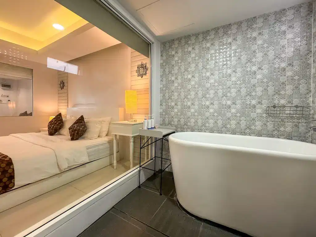 ห้องน้ำสไตล์โมเดิร์นพร้อมอ่างอาบน้ำแบบลอยตัวและผนังกระเบื้องลวดลายสวยงาม แยกจากห้องนอนด้วยหน้าต่างกระจกบานใหญ่—เหมาะสำหรับการพักผ่อนอย่างผ่อนคลายในที่พักสุดชิค น่านที่พัก.