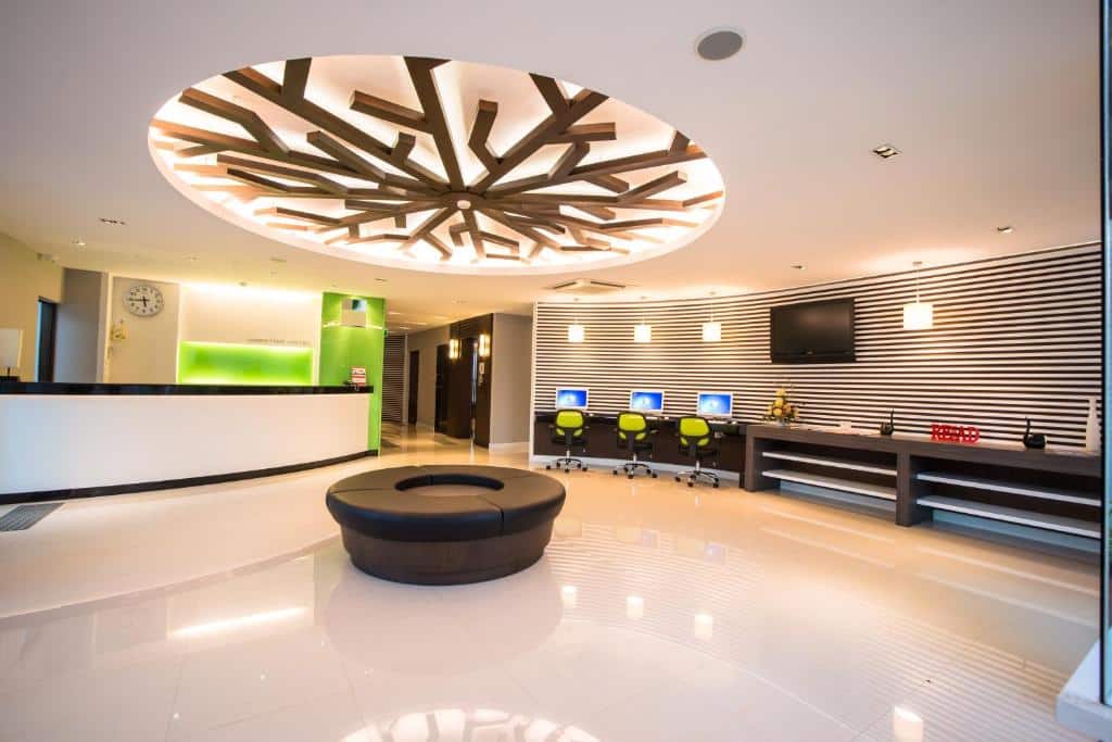 ล็อบบี้โรงแรมสมัยใหม่ที่ โรงแรมเชียงใหม่ โดดเด่นด้วยม้านั่งสีดำทรงกลม ผนังลายทาง โต๊ะทำงานคอมพิวเตอร์พร้อมเก้าอี้สีเขียว และโคมไฟเพดานตกแต่ง.