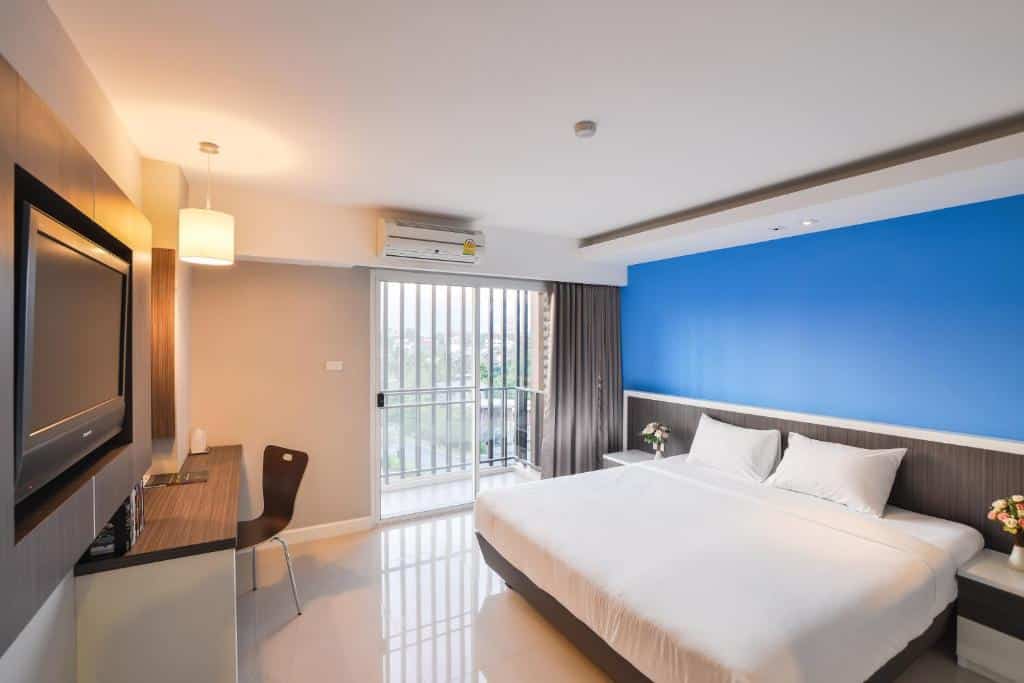 ห้องพักโรงแรมสมัยใหม่ในโรงแรมเชียงใหม่ ประกอบด้วยเตียงขนาดใหญ่ ผนังสีน้ำเงินเป็นจุดเด่น โต๊ะและเก้าอี้ ทีวีจอแบน และประตูกระจกบานเลื่อนที่เปิดออกสู่ระเบียงพร้อมวิวทิวทัศน์ที่สวยงามภายนอก.