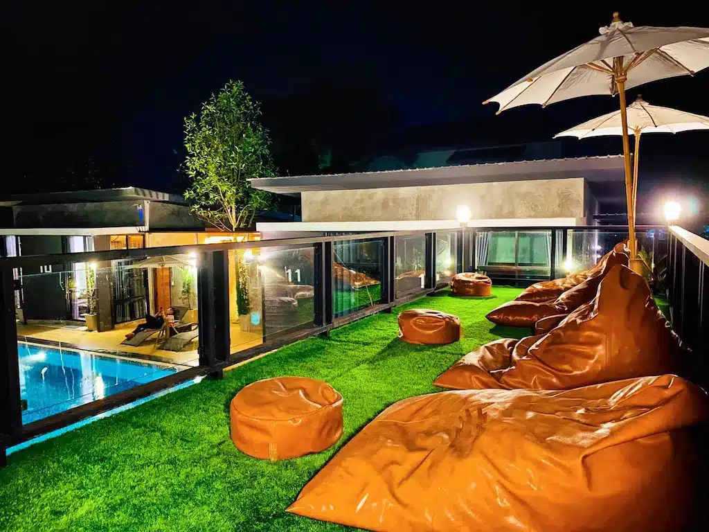 ถุงบีนบAGและร่มบนหญ้าเทียมสามารถมองเห็นสระว่ายน้ำที่สว่างไสวในยามค่ำคืน พร้อมตึกสูงสมัยใหม่และไฟส่องสว่างเป็นฉากหลัง—ที่พักน่าชวนให้มาพักผ่อนสำหรับการหนีไปผ่อนคลายของคุณ.
