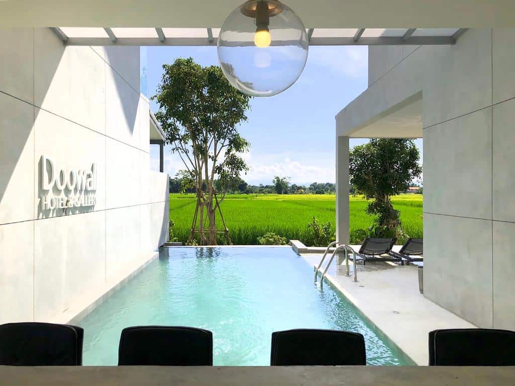 สระว่ายน้ำกลางแจ้งสมัยใหม่พร้อมเก้าอี้เลานจ์และวิวทุ่งหญ้าเขียวขจี รายล้อมด้วยอาคารสีขาวที่โรงแรมและห้องสวีท Loowa—ที่พักเชียงรายที่เหมาะสำหรับการพักผ่อนอย่างแท้จริง.