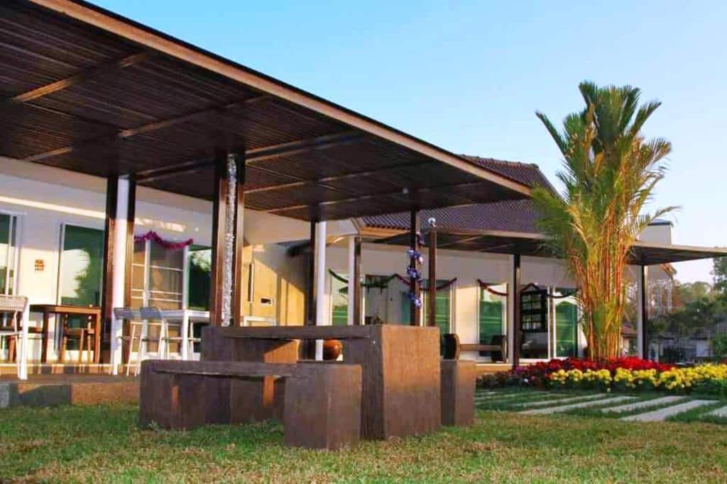 บ้านชั้นเดียวสไตล์โมเดิร์นพร้อมเฉลียงหลังคา, พื้นที่นั่งเล่นกลางแจ้ง, สนามหญ้าที่ตัดแต่งอย่างสวยงาม, และต้นไม้ประดับที่เขียวชอุ่ม—เหมาะสำหรับผู้ที่ต้องการที่พักเชียงรายหรือรีสอร์ทเชียงรายที่เงียบสงบ.