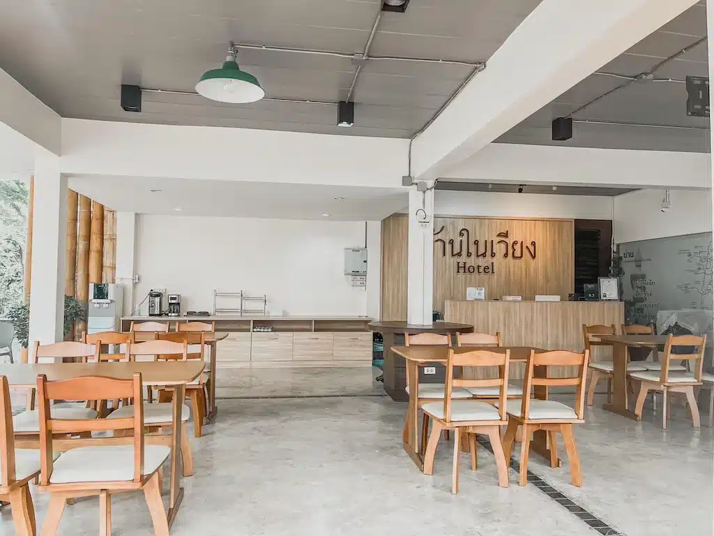 บริเวณล็อบบี้โรงแรมพร้อมเก้าอี้และโต๊ะไม้ เคาน์เตอร์ต้อนรับ และเครื่องชงกาแฟในบรรยากาศสว่างและเรียบง่าย เหมาะสำหรับผู้ที่มองหา รีสอร์ทน่าน หรือ ที่พักน่าน ทันสมัยในสไตล์และความสะดวกสบาย.