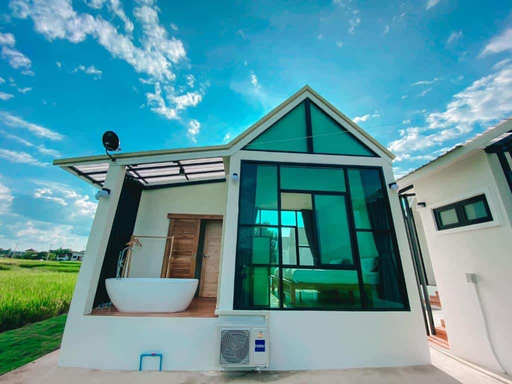 บ้านขนาดเล็กสมัยใหม่พร้อมหน้าต่างกระจกบานใหญ่ ภายในมีเตียงที่มองเห็นได้ อ่างอาบน้ำภายนอก และเครื่องปรับอากาศกลางแจ้งใต้ท้องฟ้าสดใส—ทางเลือกที่สมบูรณ์แบบสำหรับ ที่พักน่าน ที่มีความสะดวกสบายและสไตล์.