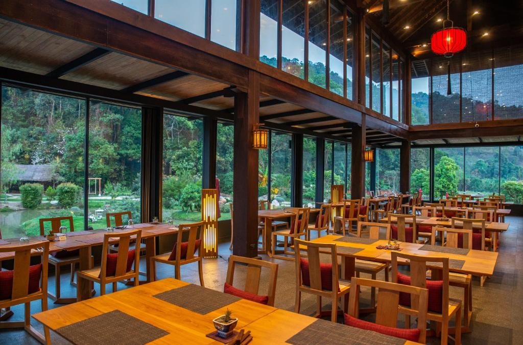 ร้านอาหารกว้างขวางพร้อมโต๊ะและเก้าอี้ไม้ หน้าต่างบานใหญ่จากพื้นจรดเพดาน และวิวสวนสีเขียวและป่าไม้—เหมาะสำหรับแขกที่ต้องการประสบการณ์รีสอร์ทเชียงใหม่ที่ผ่อนคลาย.