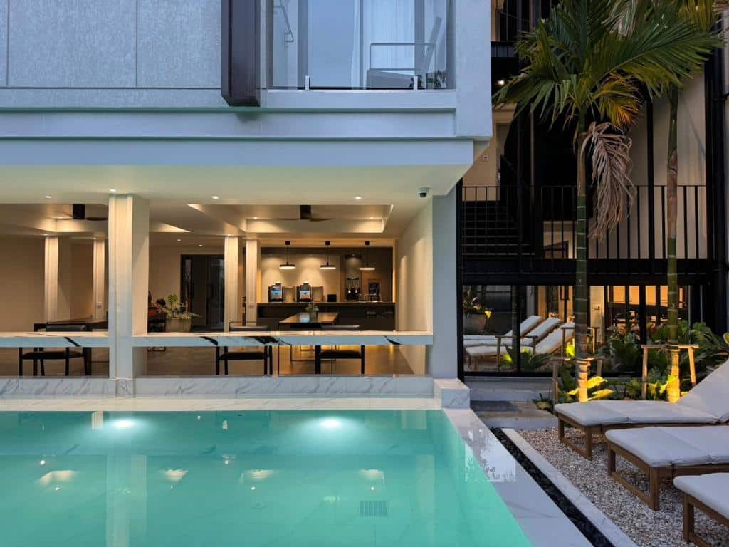 บ้านสมัยใหม่พร้อมสระว่ายน้ำ เก้าอี้เลานจ์ริมสระ ครัวเปิดโล่ง และหน้าต่างบานใหญ่ที่มองเห็นพื้นที่กลางแจ้ง เหมาะสำหรับผู้ที่ต้องการบรรยากาศรีสอร์ทเชียงใหม่ในความสะดวกสบายของบ้านคุณเอง.