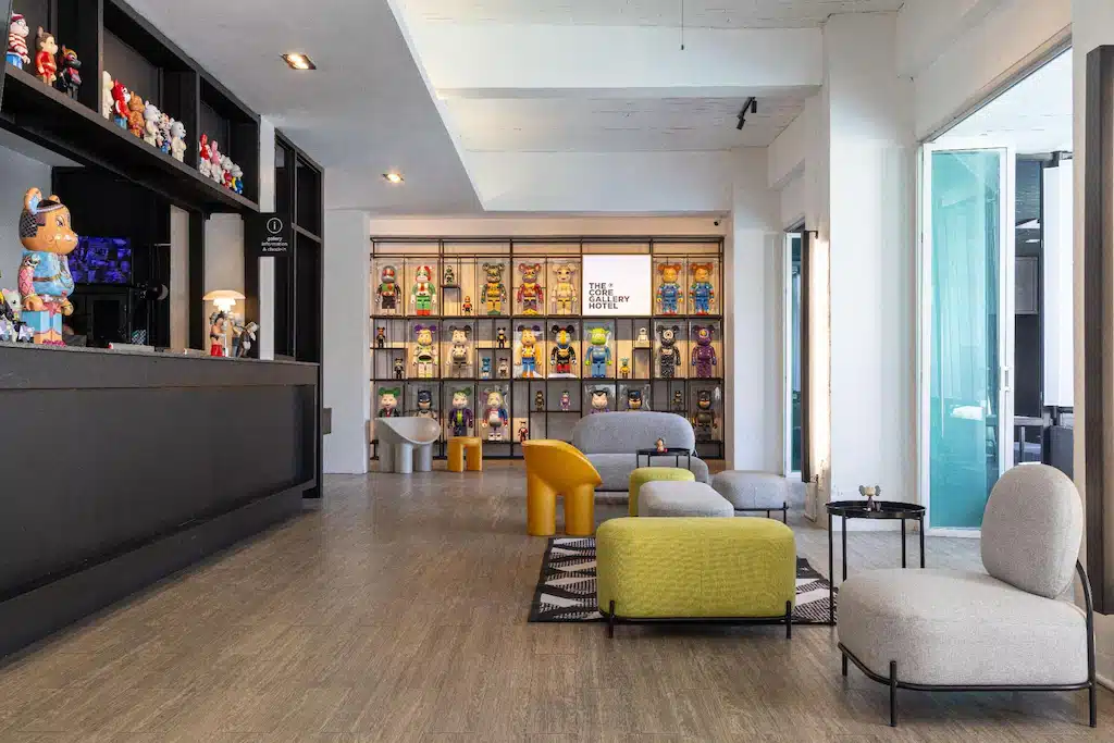 ล็อบบี้สมัยใหม่ของโรงแรมเชียงใหม่แห่งนี้มีเก้าอี้เลานจ์ พรมลายสวย โต๊ะต้อนรับสีดำเงา และชั้นวางของที่มีตุ๊กตาสะสมสีสันสดใส หน้าต่างบานใหญ่ช่วยให้ที่พักเชียงใหม่แห่งนี้เต็มไปด้วยแสงธรรมชาติ.