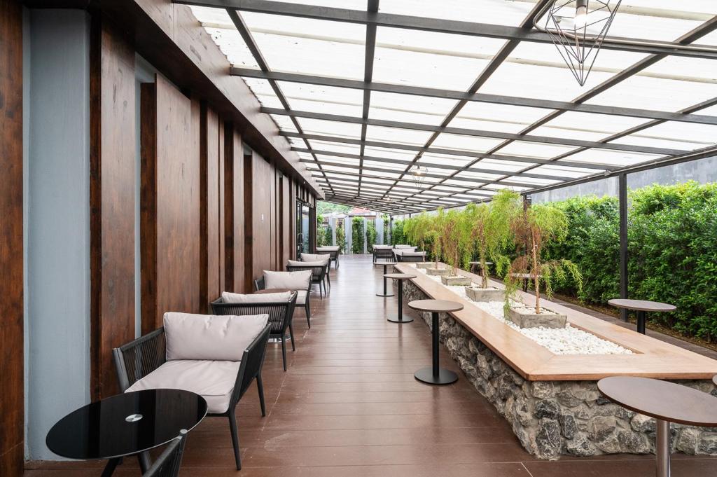 พื้นที่นั่งเล่นกลางแจ้งที่มีหลังคาคลุม พร้อมเก้าอี้บุเบาะ โต๊ะกลมขนาดเล็ก และกระถางต้นไม้ตรงกลาง—เหมาะสำหรับการพักผ่อนที่ โรงแรมเชียงราย รายล้อมด้วยผนังกระจกและพืชพรรณเขียวชอุ่ม.