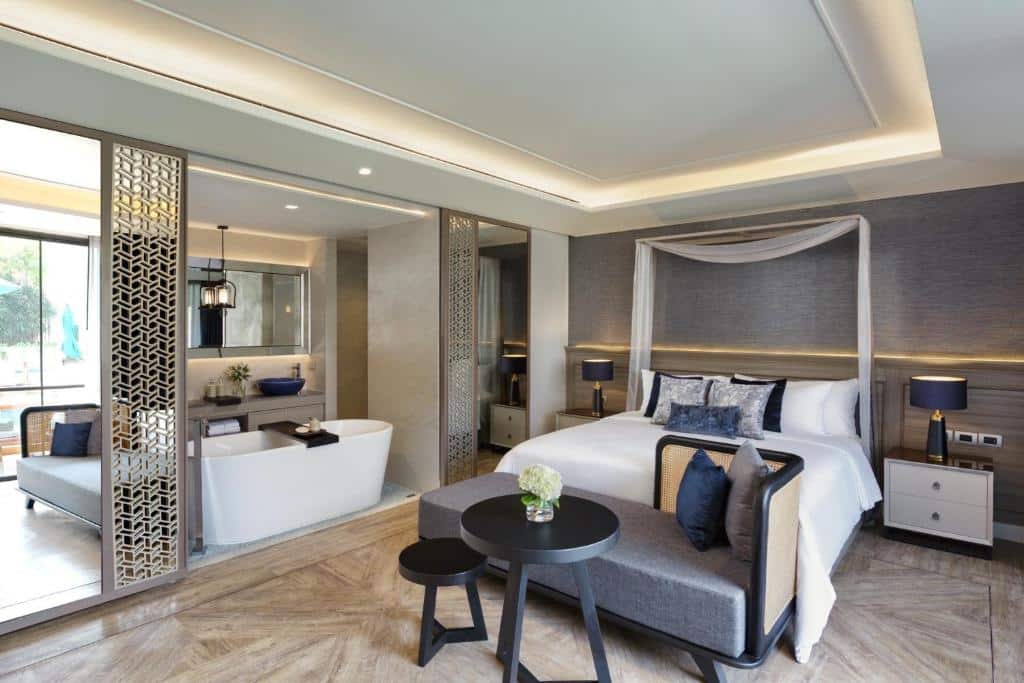 ห้องสวีทโรงแรมสมัยใหม่ที่ ที่พักเชียงใหม่ พร้อมเตียงคิงไซส์, พื้นที่นั่งเล่น, โต๊ะกลม, และห้องน้ำแบบเปิดโล่งที่มีอ่างอาบน้ำแบบลอยตัวแยกด้วยฉากกั้นตกแต่ง.