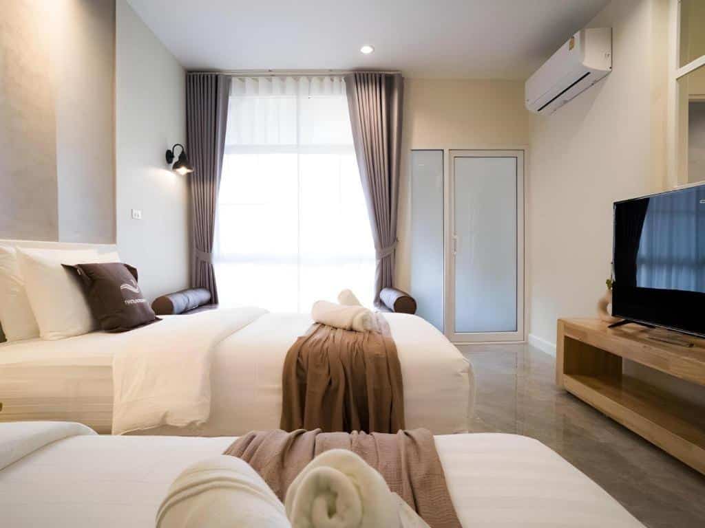 ห้องพักโรงแรมสมัยใหม่ที่ โรงแรมน่าน พร้อมเตียงสองเตียงที่จัดไว้อย่างเรียบร้อย โทรทัศน์ติดผนัง หน้าต่างพร้อมผ้าม่านยาวถึงพื้น เครื่องปรับอากาศ และการตกแต่งโทนสีเรียบ.