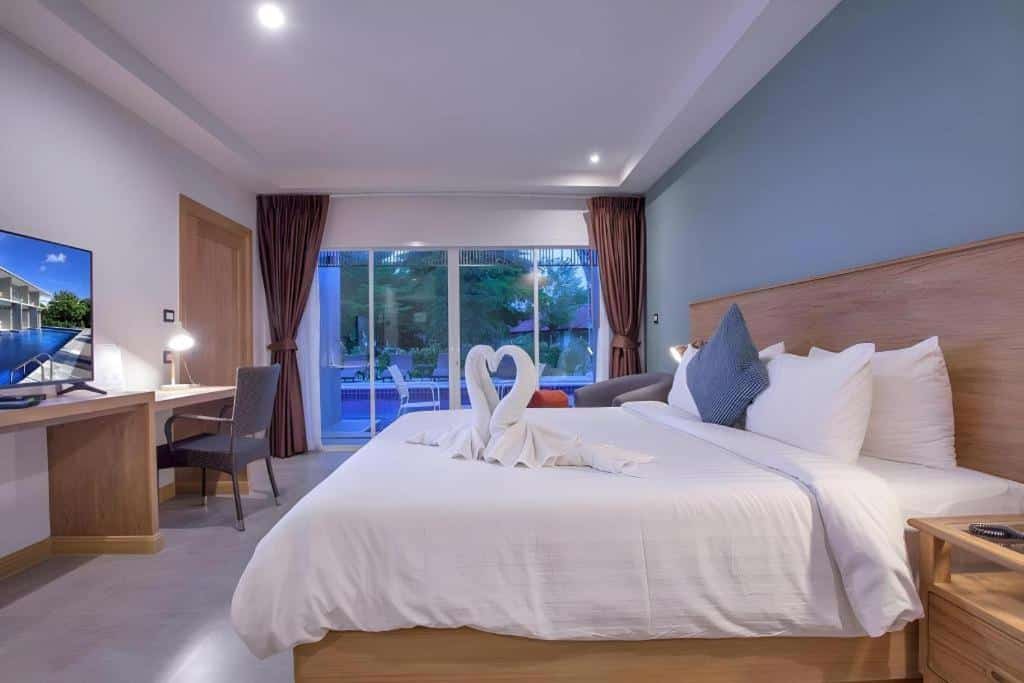 ห้องพักโรงแรมทันสมัยพร้อมเตียงขนาดใหญ่ ผ้าขนหนูรูปหงส์ โต๊ะทำงาน เก้าอี้ โทรทัศน์ และประตูกระจกบานเลื่อนที่เปิดออกสู่ระเบียงริมสระว่ายน้ำ ณ รีสอร์ทเชียงรายของเรา สำหรับการพักผ่อนที่สมบูรณ์แบบของคุณ.