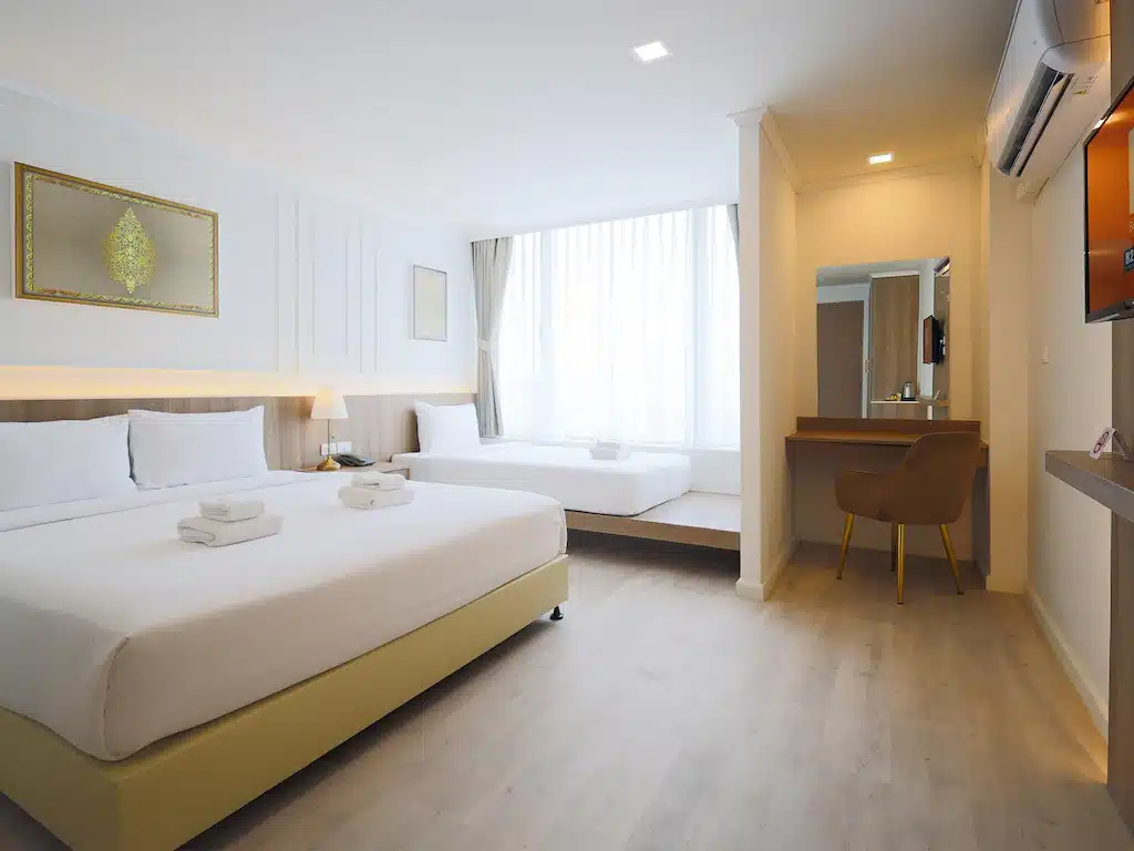 ห้องพักโรงแรมสมัยใหม่ที่ โรงแรมเชียงใหม่ พร้อมเตียงใหญ่สองเตียง ทีวีติดผนัง โต๊ะเครื่องแป้งสไตล์สวย และหน้าต่างที่ให้แสงสว่างจากธรรมชาติ. เตียงแต่ละเตียงมีผ้าเช็ดตัวพับไว้อย่างเรียบร้อยเพื่อความสะดวกสบายของคุณ.