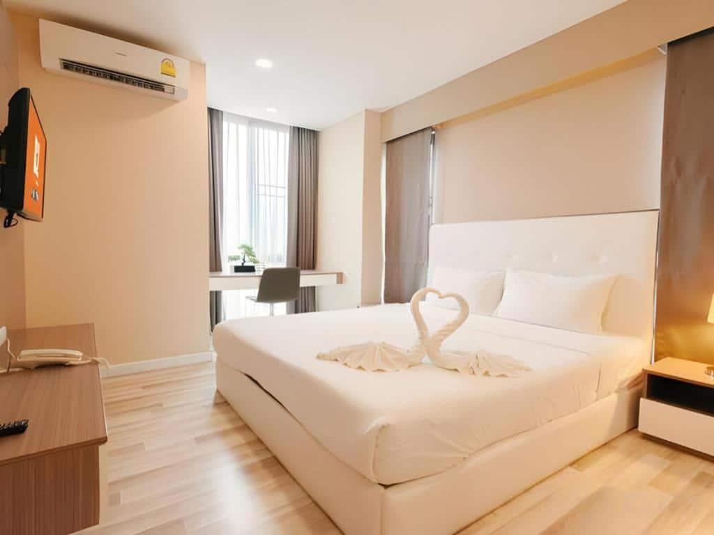 ห้องพักโรงแรมสมัยใหม่พร้อมเตียงคู่ ผ้าปูที่นอนสีขาวสะอาด ผ้าขนหนูรูปหงส์ โต๊ะและเก้าอี้ริมหน้าต่าง โคมไฟข้างเตียง และทีวีติดผนัง—เหมาะสำหรับการเข้าพักที่ โรงแรมเชียงใหม่ ของคุณ.