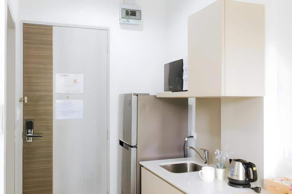 พื้นที่ครัวขนาดกะทัดรัดพร้อมตู้เย็น, ไมโครเวฟ, อ่างล้างจาน, กาต้มน้ำไฟฟ้า, ถ้วย และเครื่องใช้ต่าง ๆ อยู่ถัดจากประตูที่ปิดสนิท พื้นที่สะอาดและสว่างไสว เหมาะสำหรับการเข้าพักที่ โรงแรมเชียงราย หรือ รีสอร์ทเชียงราย.