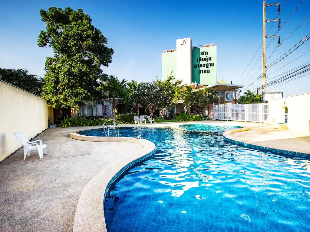 สระว่ายน้ำกลางแจ้งที่มีน้ำสีฟ้าใสสะอาด ล้อมรอบด้วยต้นไม้และอาคารต่างๆ ที่ โรงแรมเชียงใหม่ พร้อมเก้าอี้ริมสระสีขาวและท้องฟ้าสดใสแจ่มใส.