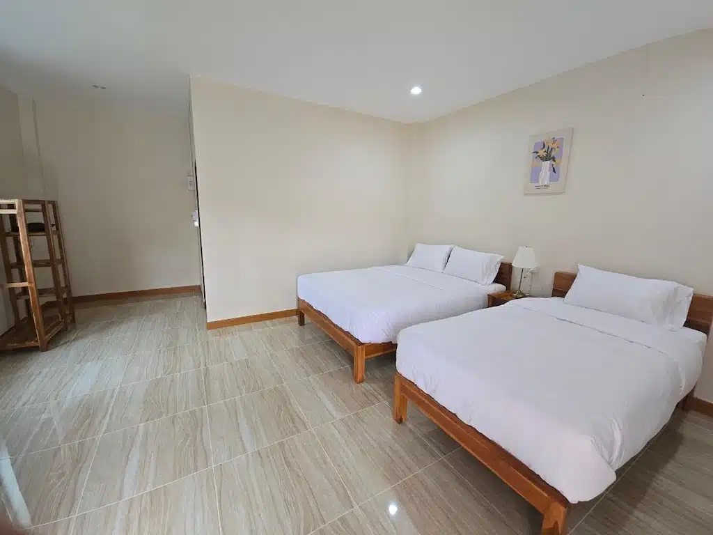 ห้องพักโรงแรมพร้อมเตียงคู่สองเตียง ชุดเครื่องนอนสีขาว โต๊ะข้างเตียงพร้อมโคมไฟ ชั้นวางของไม้ พื้นกระเบื้อง—เหมาะสำหรับผู้ที่มองหาที่พักในน่านหรือรีสอร์ทในน่านสำหรับการพักผ่อนอย่างแท้จริง.