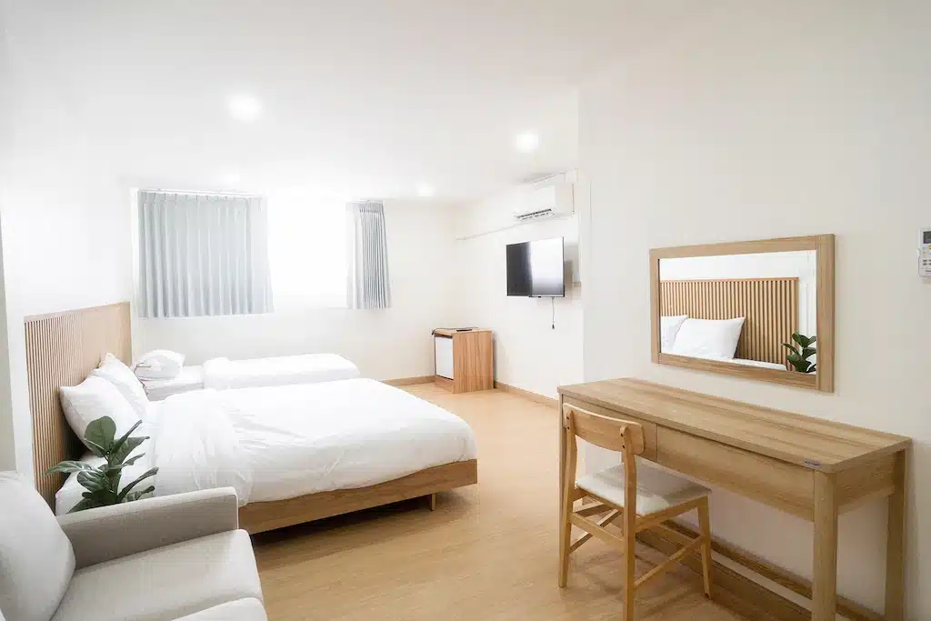 ห้องพักสไตล์มินิมอลที่โรงแรมนาน พร้อมเตียงเดี่ยวสองเตียง โต๊ะทำงานและกระจก ทีวีติดผนัง ตู้เย็นขนาดเล็ก เฟอร์นิเจอร์ไม้สีอ่อน และหน้าต่างบานใหญ่พร้อมผ้าม่านบาง เหมาะสำหรับการพักผ่อนอย่างอบอุ่นในจังหวัดน่าน.