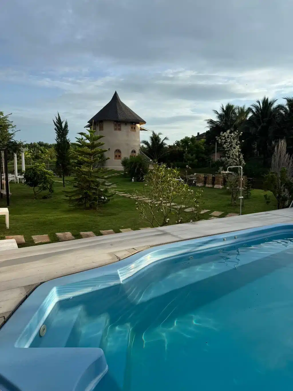 บ้านทรงกลมหลังคาทรงกรวยตั้งอยู่ในสวนสีเขียว มองเห็นจากข้างสระว่ายน้ำใต้ท้องฟ้าที่มีเมฆบางส่วน—เป็นภาพที่งดงามท่ามกลางสถานที่ท่องเที่ยวชั้นนำของเขาใหญ่สำหรับการพักผ่อน.