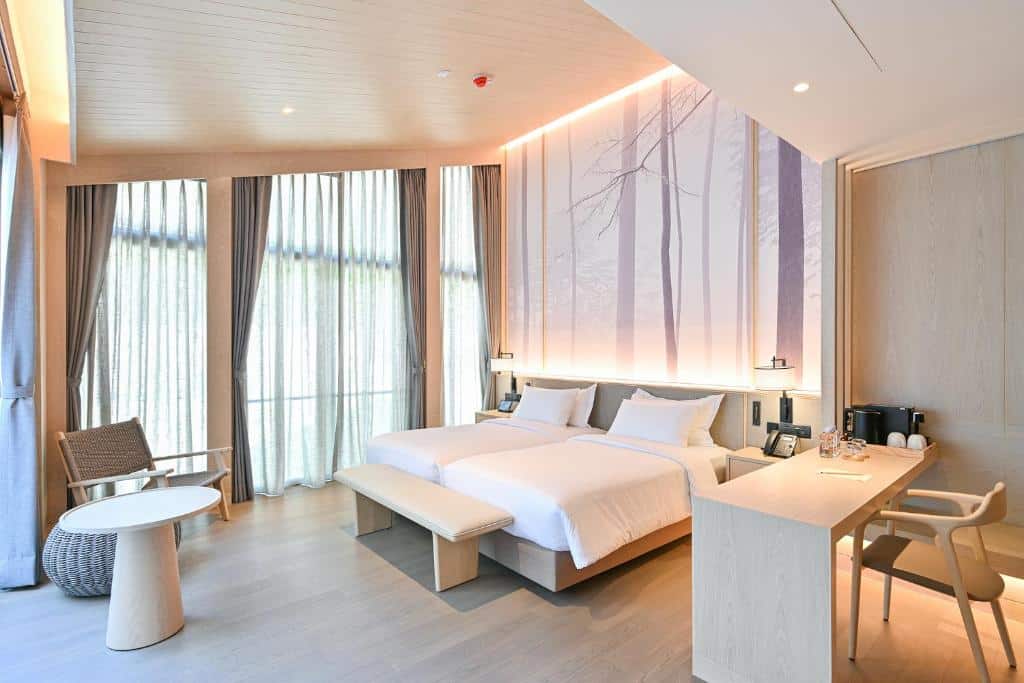 ห้องพักโรงแรมสมัยใหม่พร้อมเตียงคู่สองเตียง เฟอร์นิเจอร์ไม้สีอ่อน หน้าต่างบานใหญ่จากพื้นจรดเพดาน และภาพจิตรกรรมฝาผนังที่มีเงาของต้นไม้—เหมาะสำหรับการพักผ่อนหลังจากสำรวจสถานที่ท่องเที่ยวเขาใหญ่หรือค้นพบสถานที่ท่องเที่ยวเขาใหญ่ใกล้เคียง.