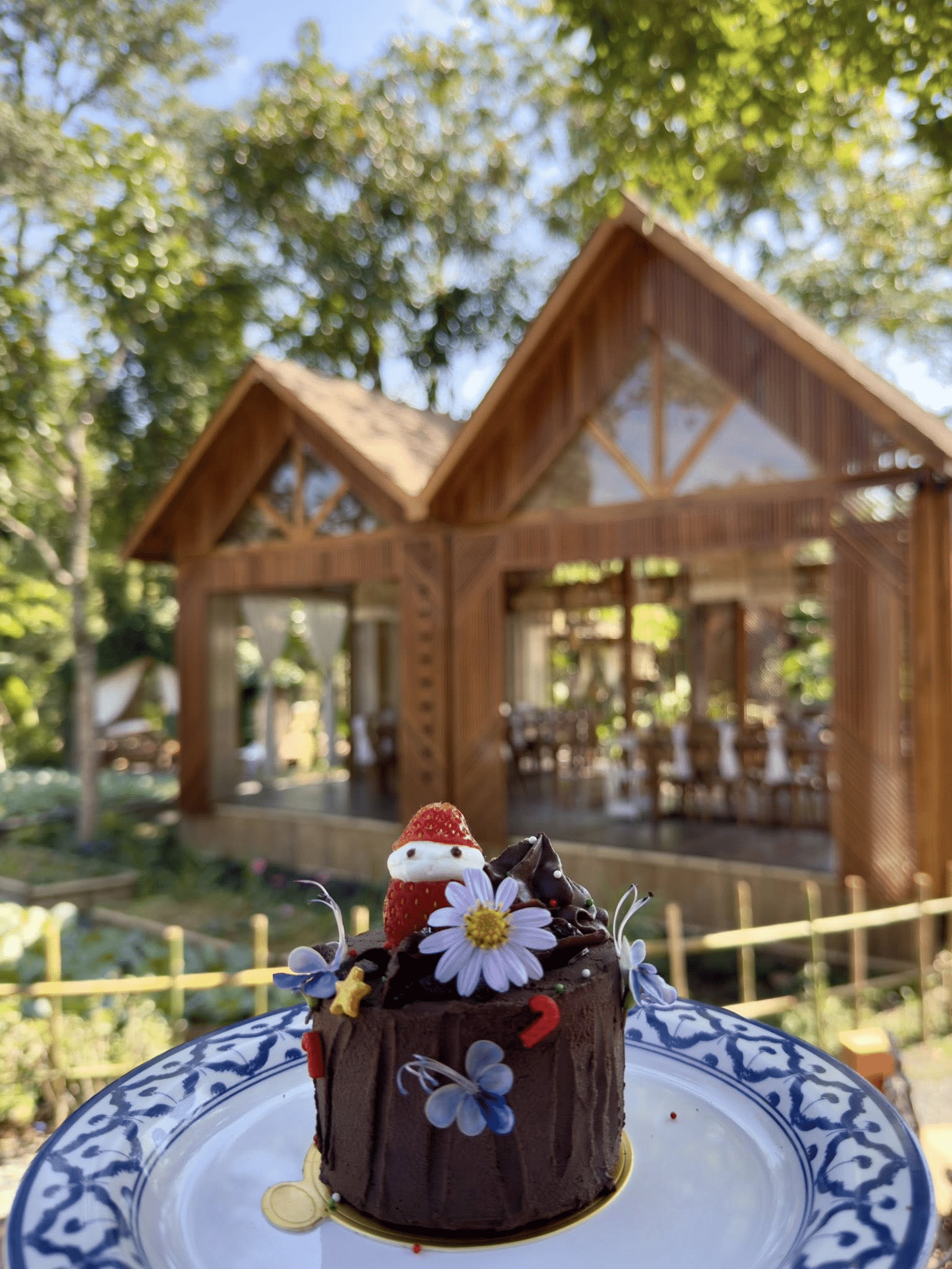 ของหวานช็อกโกแลตที่ตกแต่งด้วยดอกไม้ที่รับประทานได้และหมวกซานต้าสตรอว์เบอร์รี่บนจานตกแต่ง วางไว้เบื้องหลังอาคารไม้และพืชพรรณสีเขียว—เหมาะอย่างยิ่งสำหรับทริปผจญภัยครั้งต่อไปของคุณที่ เขาใหญ่.