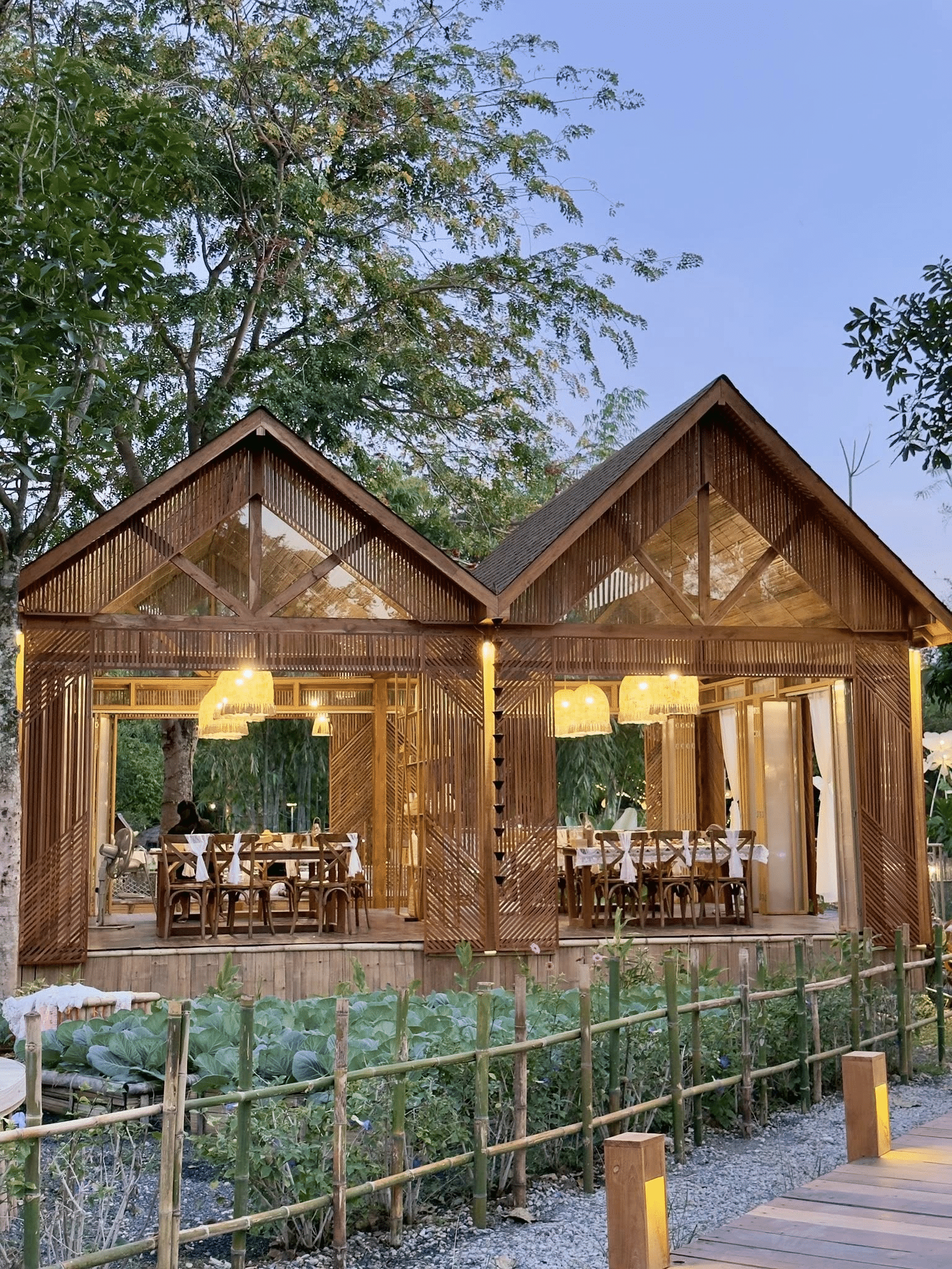 ศาลาไม้เปิดสองหลังที่มีผนังไม้ระแนงและไฟแก้วภายใน ตั้งอยู่ท่ามกลางต้นไม้และพืชพรรณเขียวขจี พร้อมโต๊ะและเก้าอี้สำหรับรับประทานอาหาร—เหมาะอย่างยิ่งสำหรับการพักผ่อนขณะเที่ยวเขาใหญ่หรือสำรวจสถานที่ท่องเที่ยวในเขาใหญ่.