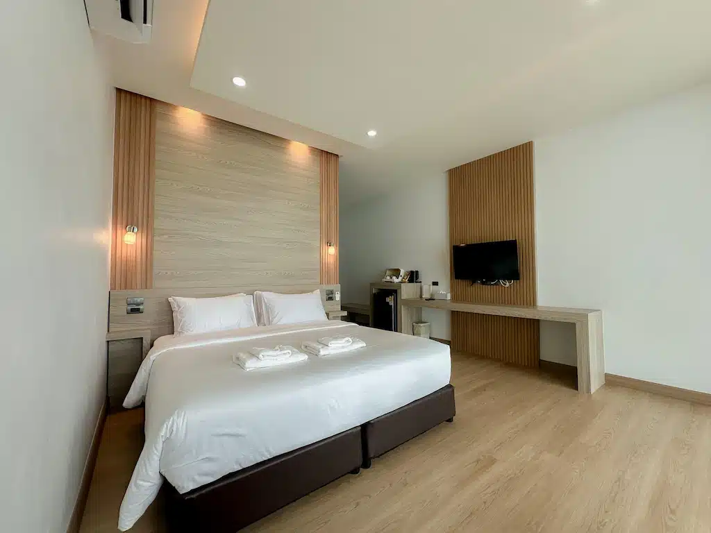 ห้องพักโรงแรมสมัยใหม่ที่ ขนอมที่พัก ประกอบด้วยเตียงคู่ที่จัดไว้อย่างเรียบร้อย ผ้าขนหนูสองผืนวางไว้ด้านบน โทรทัศน์ติดผนัง โต๊ะทำงาน และตกแต่งด้วยไม้สไตล์ทันสมัยบนผนังและพื้น.