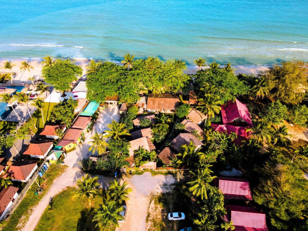 ภาพมุมสูงของหมู่บ้านชายฝั่งที่มีบ้านเรือน, ที่พักขนอม ซ่อนตัวอยู่ท่ามกลางต้นปาล์ม, ชายหาดทราย, และคลื่นทะเลสีฟ้าคราม.