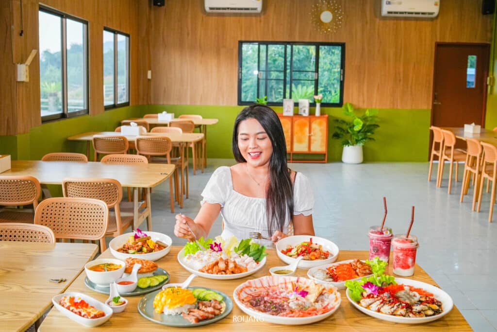 ผู้หญิงคนหนึ่งนั่งอยู่ที่โต๊ะในร้าน เพาะรัก ซึ่งเป็นร้านอาหารที่กว้างขวางและทันสมัย มีจานอาหารและเครื่องดื่มหลายจานจัดเรียงอยู่ตรงหน้าเธอ.