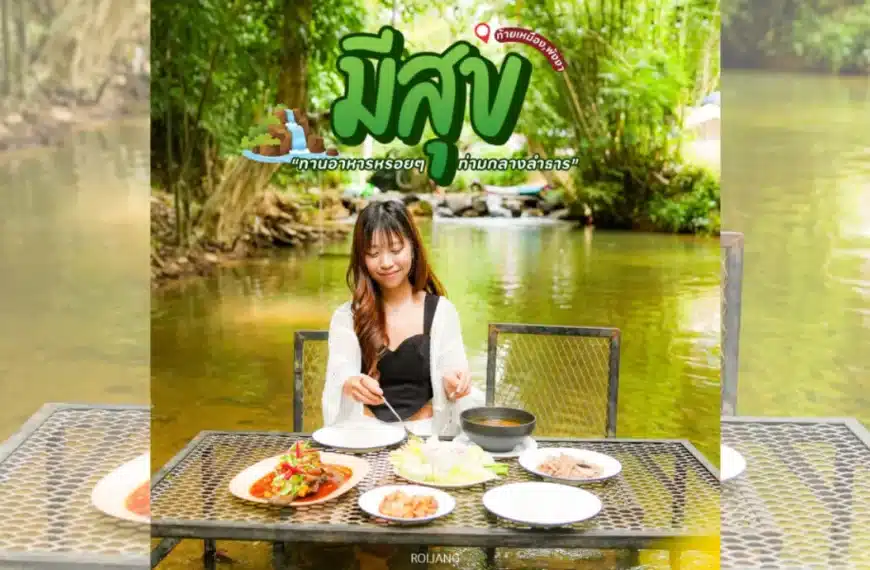 ผู้หญิงคนหนึ่งนั่งอยู่คนเดียวที่โต๊ะซึ่งจัดเตรียมอาหารหลากหลายไว้รอบตัว นั่งรับประทานอาหารกลางแจ้งริมลำธารที่รายล้อมไปด้วยต้นไม้เขียวชอุ่ม เพลิดเพลินกับช่วงเวลาแห่งความสุขท่ามกลางความสงบของธรรมชาติ.