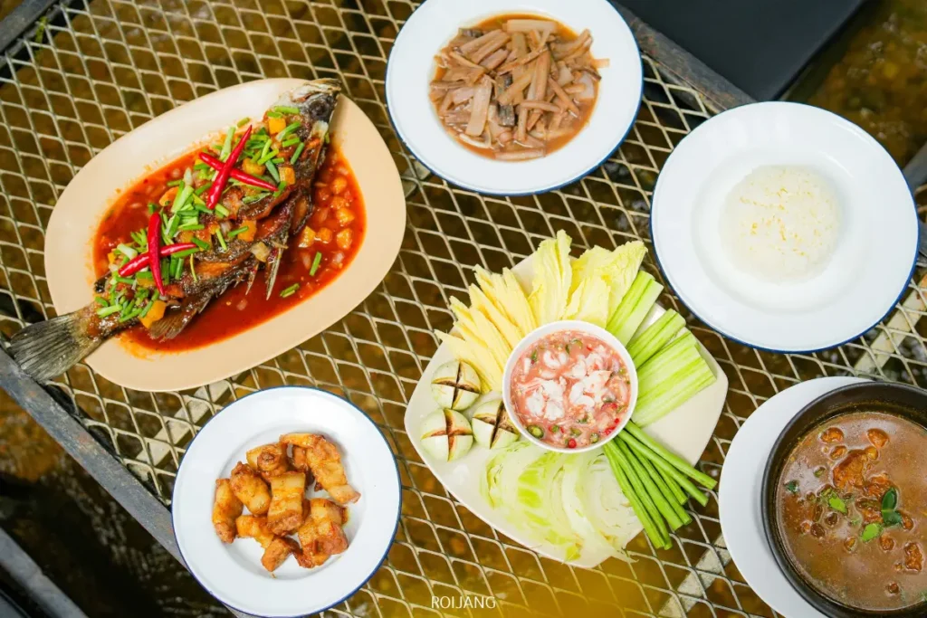 โต๊ะที่มีจานปลาปรุงรสในซอส, เนื้อหั่นบาง, ชิ้นทอด, ข้าว, ชามซุป, และจานผักสดพร้อมน้ำจิ้ม—เหมาะสำหรับการแบ่งปันและสร้างช่วงเวลาแห่งความสุขร่วมกัน.