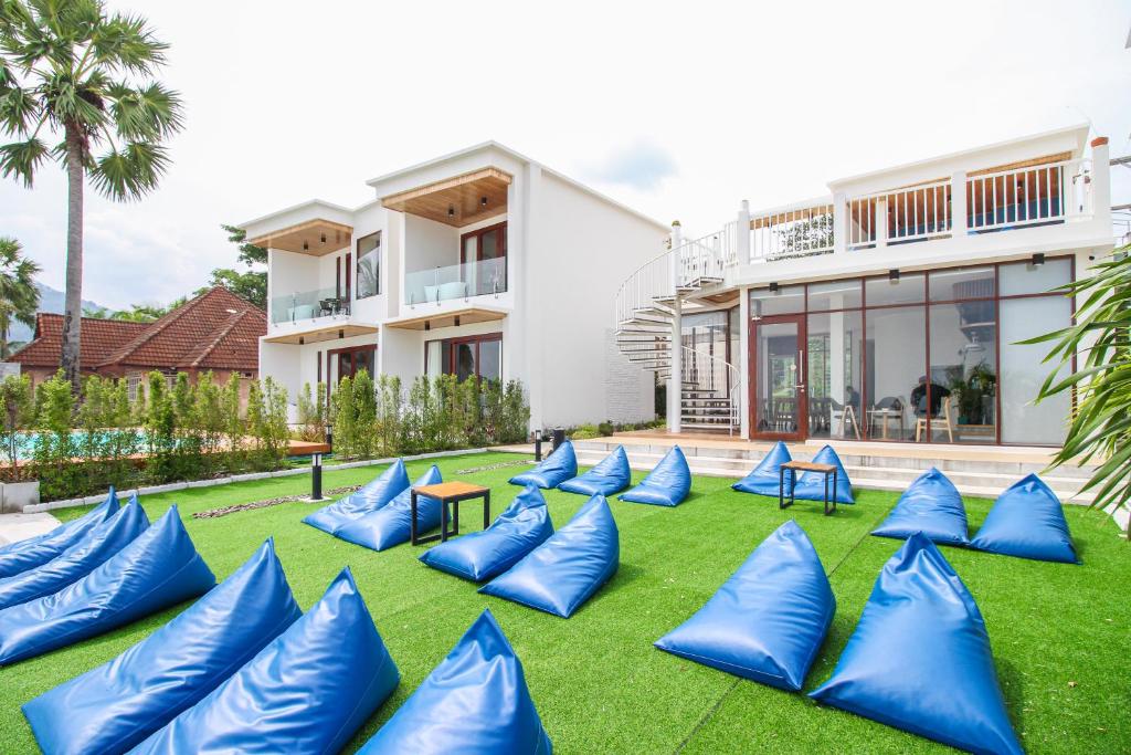 อาคารสีขาวสมัยใหม่สองชั้น มีเก้าอี้บีนแบ็กสีน้ำเงินบนสนามหญ้าเทียมสีเขียว บันไดวน และพื้นที่นั่งเล่นกลางแจ้งในสวนที่จัดแต่งอย่างสวยงาม—เหมาะอย่างยิ่งสำหรับผู้ที่มองหา โรงแรมขนอม หรือ ที่พักขนอม ที่มีสไตล์.