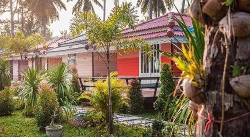 แถวของบ้านพักขนาดเล็กสีสันสดใสหลังคาสีแดง ล้อมรอบด้วยต้นปาล์มและพืชพรรณเขียวชอุ่มในบรรยากาศเขตร้อน เหมาะอย่างยิ่งสำหรับผู้ที่มองหาที่พักในขนอมที่เงียบสงบหรือรีสอร์ทในขนอมเพื่อการพักผ่อนอย่างแท้จริง.