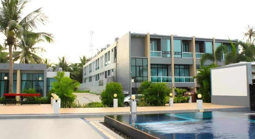 โรงแรมขนอมสองชั้นสมัยใหม่พร้อมหน้าต่างบานใหญ่ ภูมิทัศน์สีเขียว และสระว่ายน้ำกลางแจ้งอยู่ด้านหน้า.