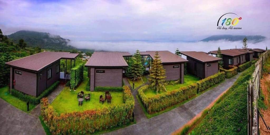 แถวของบ้านพักสมัยใหม่หลังคาสีน้ำตาลตั้งอยู่บนเนินเขา มองเห็นหุบเขาที่ปกคลุมด้วยหมอกและภูเขาไกลๆ ล้อมรอบด้วยพื้นที่สีเขียว—ที่พักเพชรบูรณ์ที่เหมาะสำหรับผู้ที่มองหาความสงบและวิวทิวทัศน์อันงดงาม.