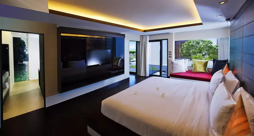 ห้องพักโรงแรมสมัยใหม่พร้อมเตียงขนาดใหญ่ ทีวีติดผนัง พื้นที่นั่งเล่นริมหน้าต่าง และวิวสระว่ายน้ำส่วนตัวและพื้นที่สีเขียว—เหมาะสำหรับการพักผ่อนที่รีสอร์ทขนอม.