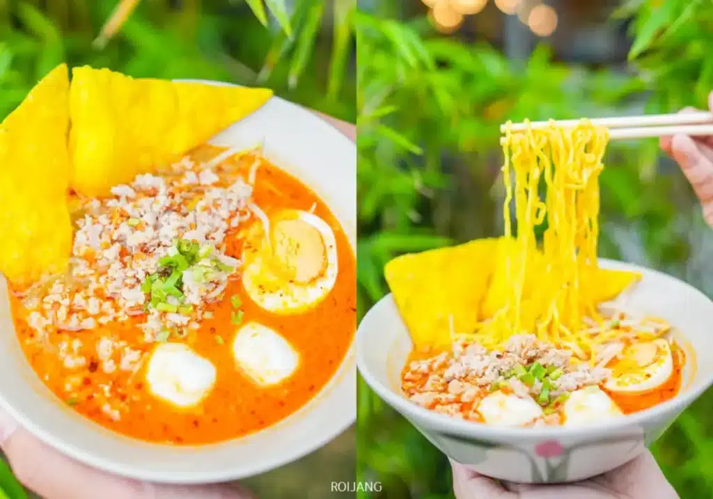 ชามบะหมี่น้ำซุปเผ็ดจากร้าน Bear Grill โรยหน้าด้วยไข่ต้มผ่าครึ่ง เนื้อสับ เกี๊ยวทอดกรอบสีเหลือง และต้นหอมซอย—ถ่ายแบบโคลสอัพพร้อมเส้นบะหมี่ที่ยกขึ้นด้วยตะเกียบ.