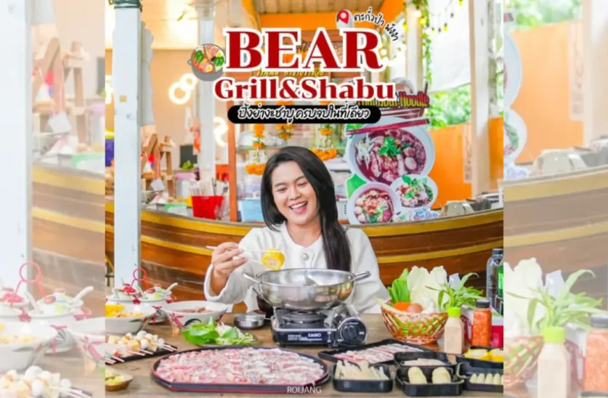 บุคคลหนึ่งนั่งอยู่ที่โต๊ะพร้อมด้วยวัตถุดิบสำหรับชาบูชาบูและปิ้งย่างหลากหลายชนิด ยิ้มและกำลังปรุงอาหารที่ร้าน Bear Grill & Shabu.