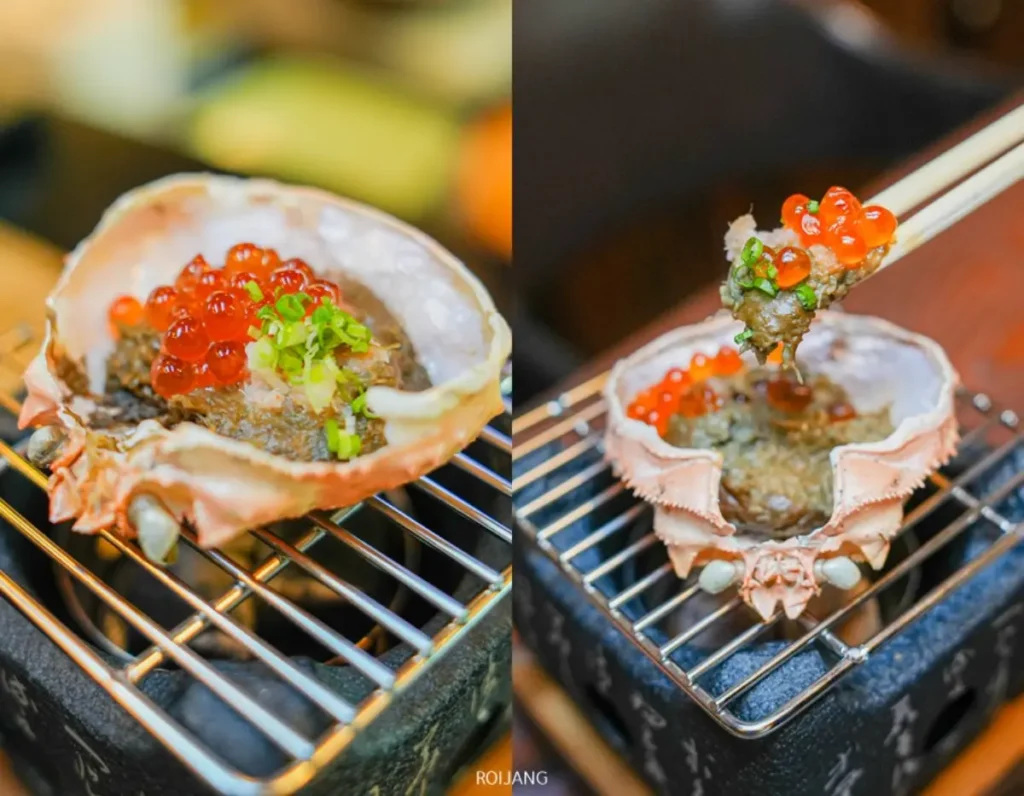 เปลือกปูที่บรรจุอาหารทะเลเต็ม พร้อมด้วยไข่ปลาแซลมอนและต้นหอม โรยด้านบน ย่างจนสุกพอดีที่ JAPs ตะกั่วป่า และแสดงให้เห็นว่ากำลังถืออย่างประณีตด้วยตะเกียบ.