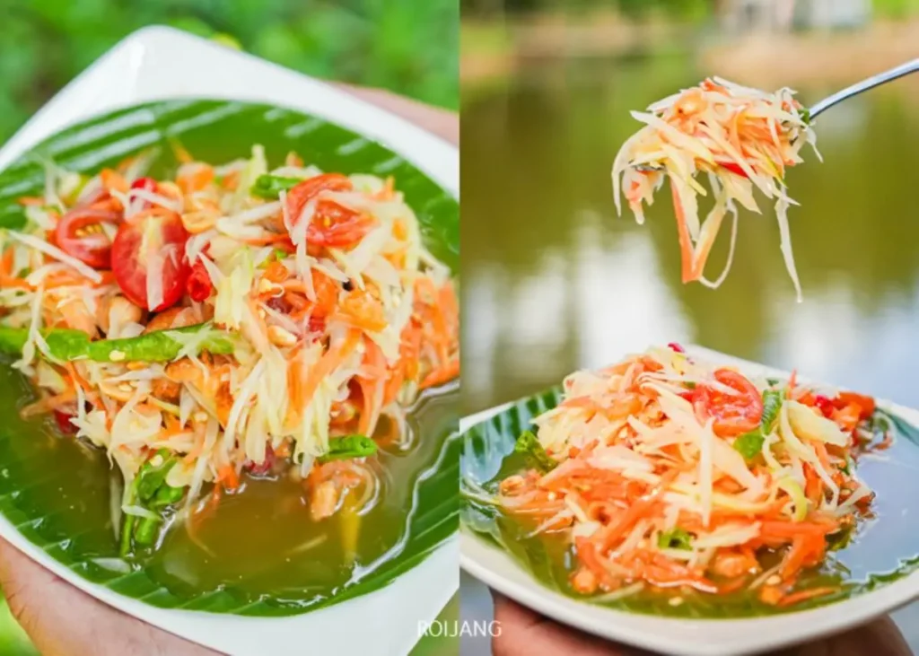 จานสลัดมะละกอไทยพร้อมผักสับและมะเขือเทศ เสิร์ฟบนใบตอง วางอยู่ในอากาศบริสุทธิ์ของหุบเขาหมอก ถัดจากส้อมที่ถือสลัดไว้เหนือจานในบรรยากาศกลางแจ้ง.