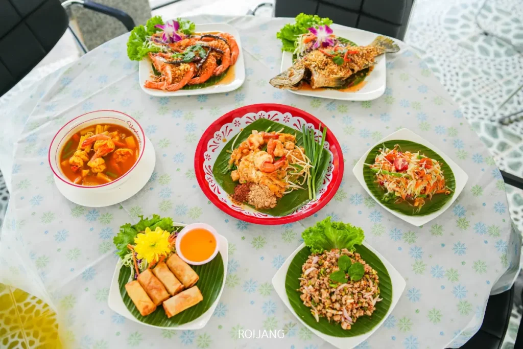 โต๊ะที่จัดวางอาหารไทยหลากหลายชนิด ตั้งแต่ปลาทอดและปูทั้งตัวไปจนถึงปอเปี๊ยะทอด ข้าวผัด ส้มตำ และแกงถ้วย—เหมาะสำหรับการลิ้มรสชาติที่แท้จริงในบรรยากาศอันเงียบสงบของหุบเขาหมอก.