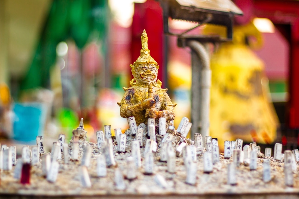 รูปปั้นทองคำขนาดเล็กของตัวละครในตำนานล้อมรอบด้วยแถวของไม้ตั้งตรงที่มีตัวเลข สร้างฉากที่ไม่ ที่เที่ยวใกล้กรุงเทพ เหมือนใครเหมาะสำหรับผู้ที่มองหา ที่เที่ยวใกล้กรุงเทพ ในบรรยากาศกลางแจ้ง.