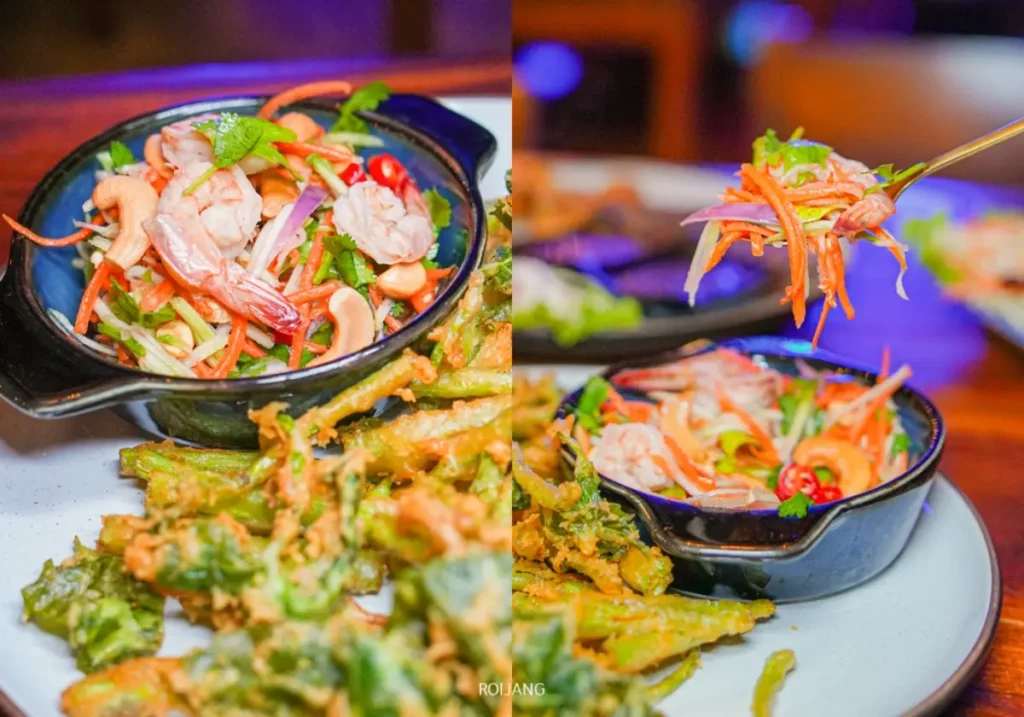 ชามสลัดกุ้งพร้อมผักหั่นบางและพริกวางอยู่ข้างจานผักทอดกรอบบนจานสีขาว พร้อมให้คุณเพลิดเพลินที่ The Rooftop.