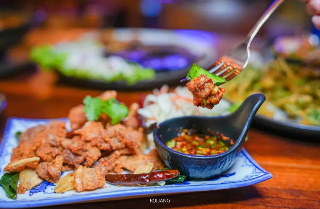 ส้อมถือชิ้นเนื้อทอดไว้เหนือจานที่มีเนื้อทอด ผัก และชามเล็ก ๆ ของน้ำจิ้มรสเผ็ดที่ The Rooftop.